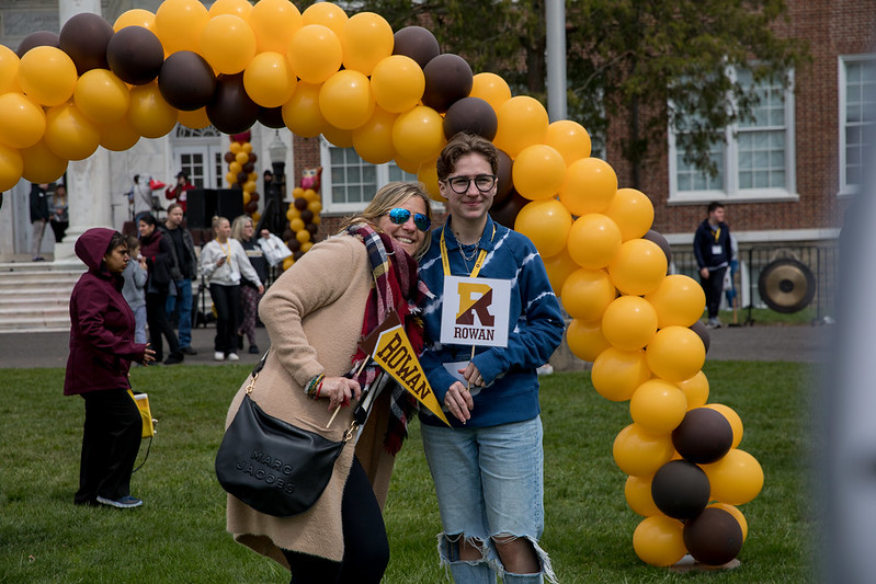 A mother and son smile happily under a brown and gold school color balloon arch at Rowan University accepted students day. 