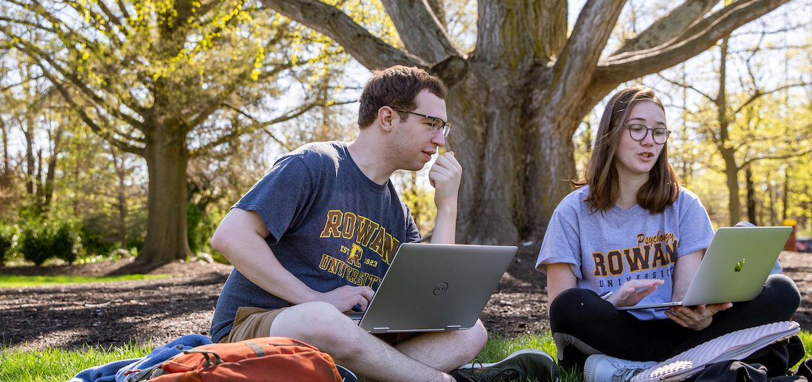 A male and female student sit under a tree at Rowan University studying.