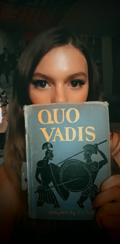 Katelyn holds an adaptation of Quo Vadis in front of her face covering the lower half. 