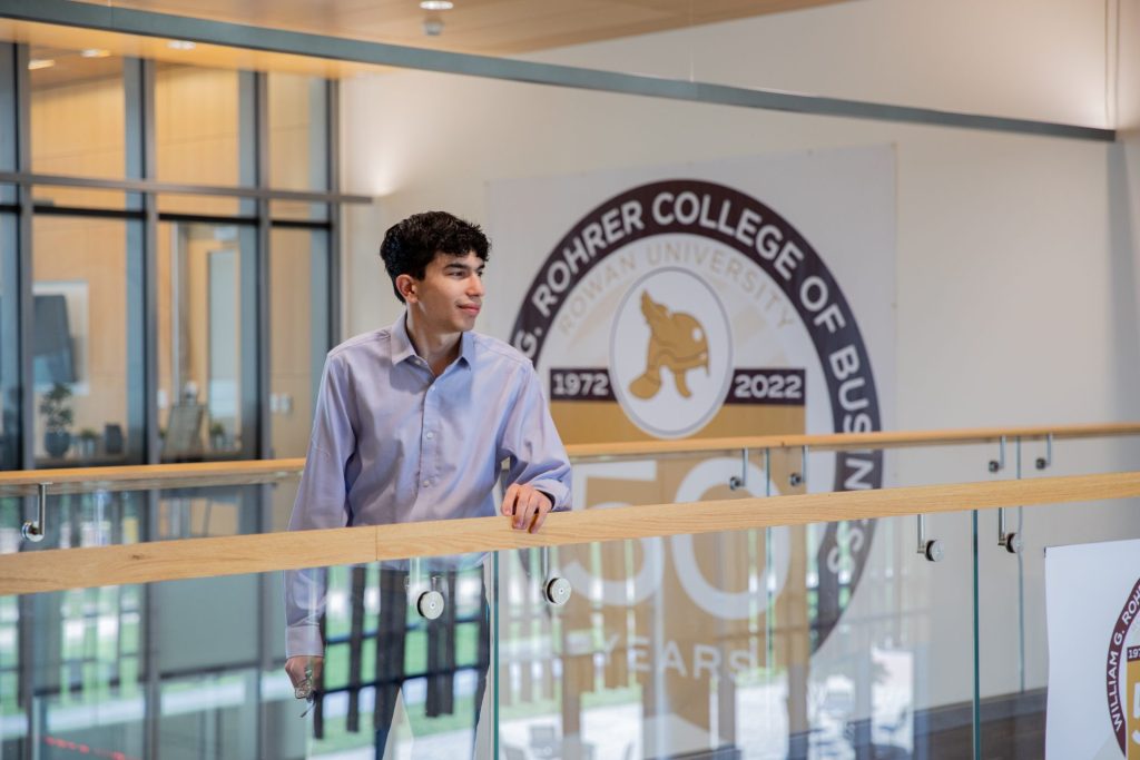 Trevor stands in the Business Building with a 50th anniversary logo behind him. 