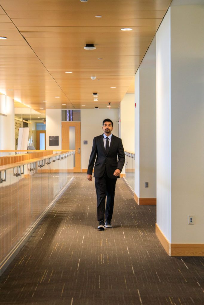 Somyaranjan Rout walks down the hall in business hall, while wearing a business suit. 