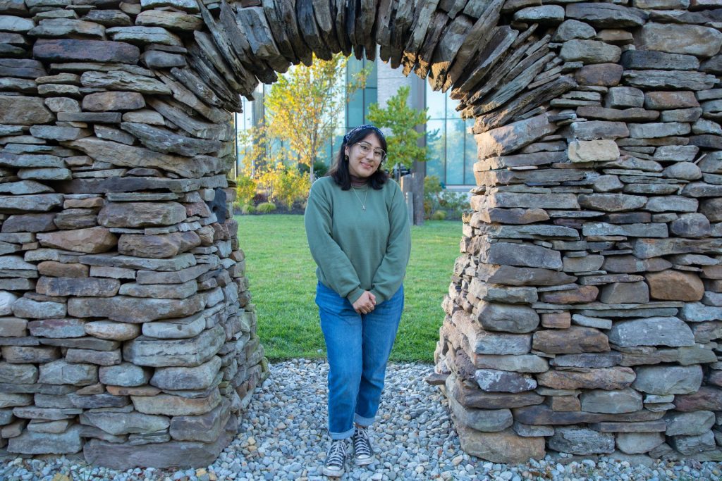 Kathleen poses under a student-created rock arch art installation. 