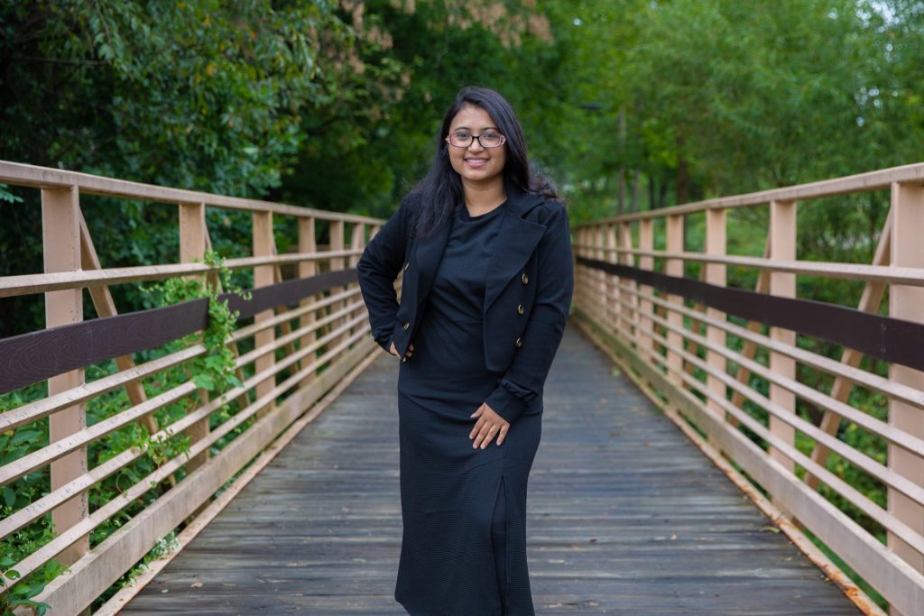 Tilpa stands with her hand on her hip on a bridge on campus, surrounded by green foliage. 