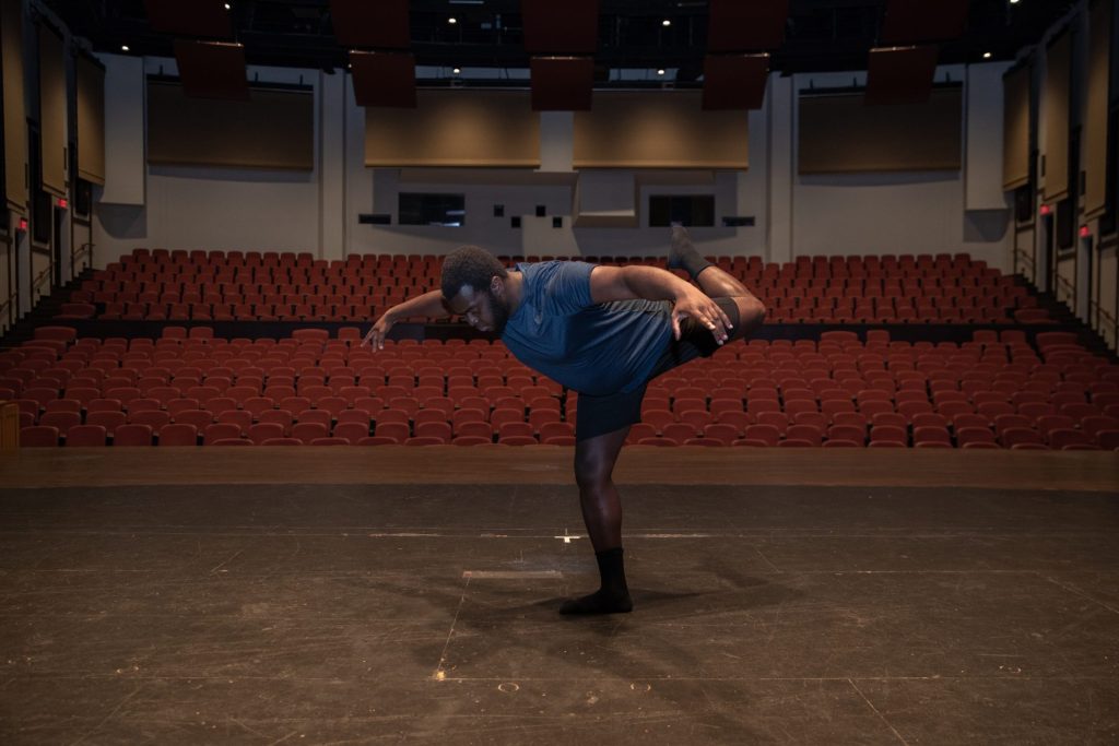 Gregory balances on one foot in a dance move in the theatre. 
