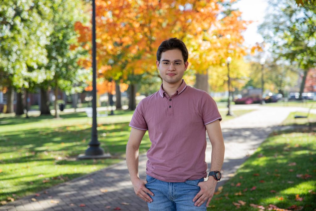 Nathaneal stands for a portrait with the backdrop of autumn leaves behind him.