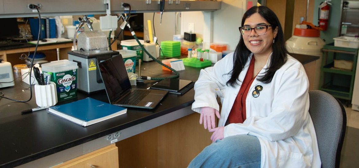 Yesenia sits at a lab table for a portrait.