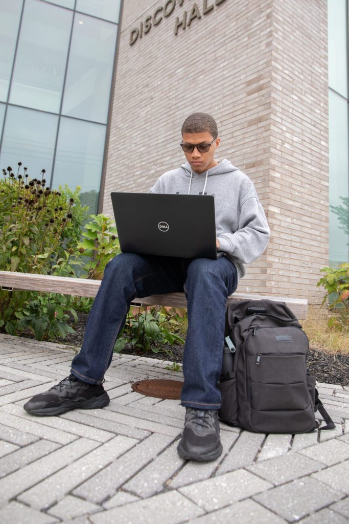 Rowan University computer science major Steven Warner sitting outside of Discovery Hall with his laptop. 