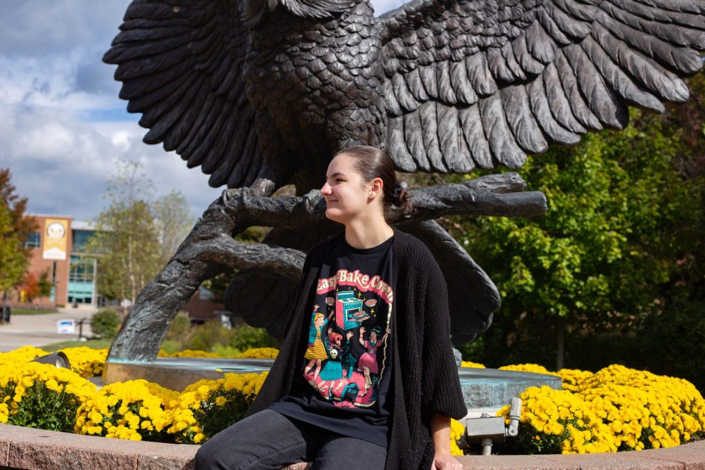 Alianna Bronstein sitting outside, with the Rowan Prof statue in the background.