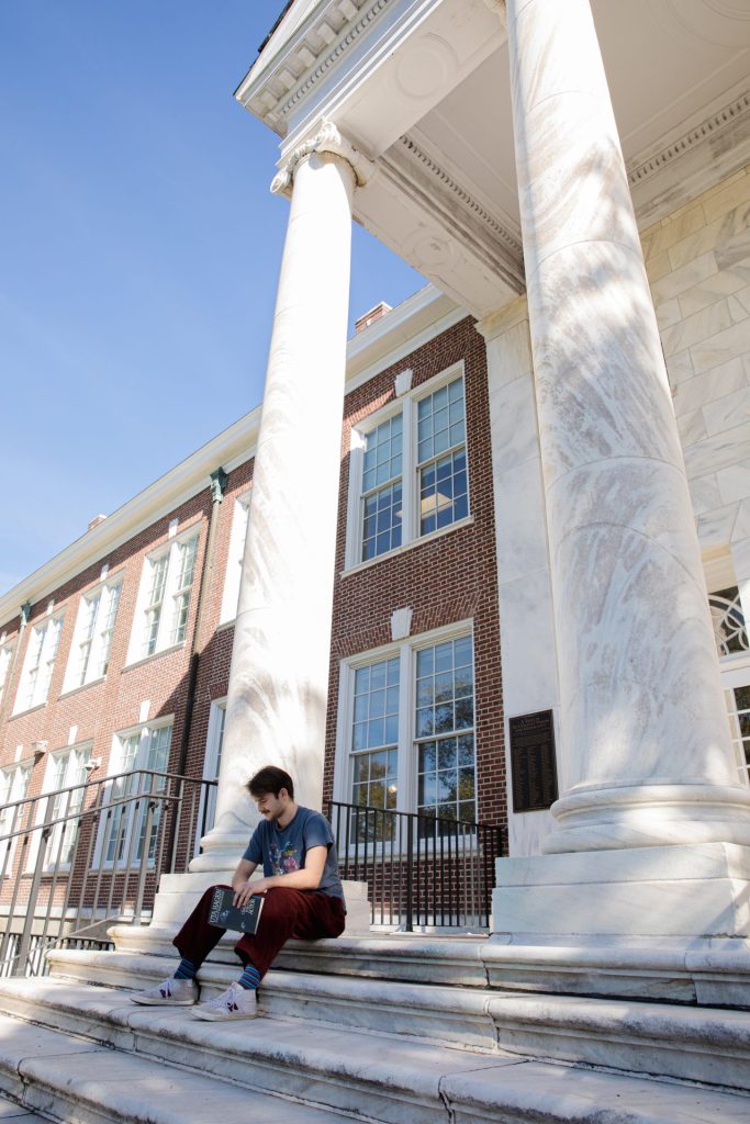 A male student in 2023 sits on Bunce steps holding a book. 