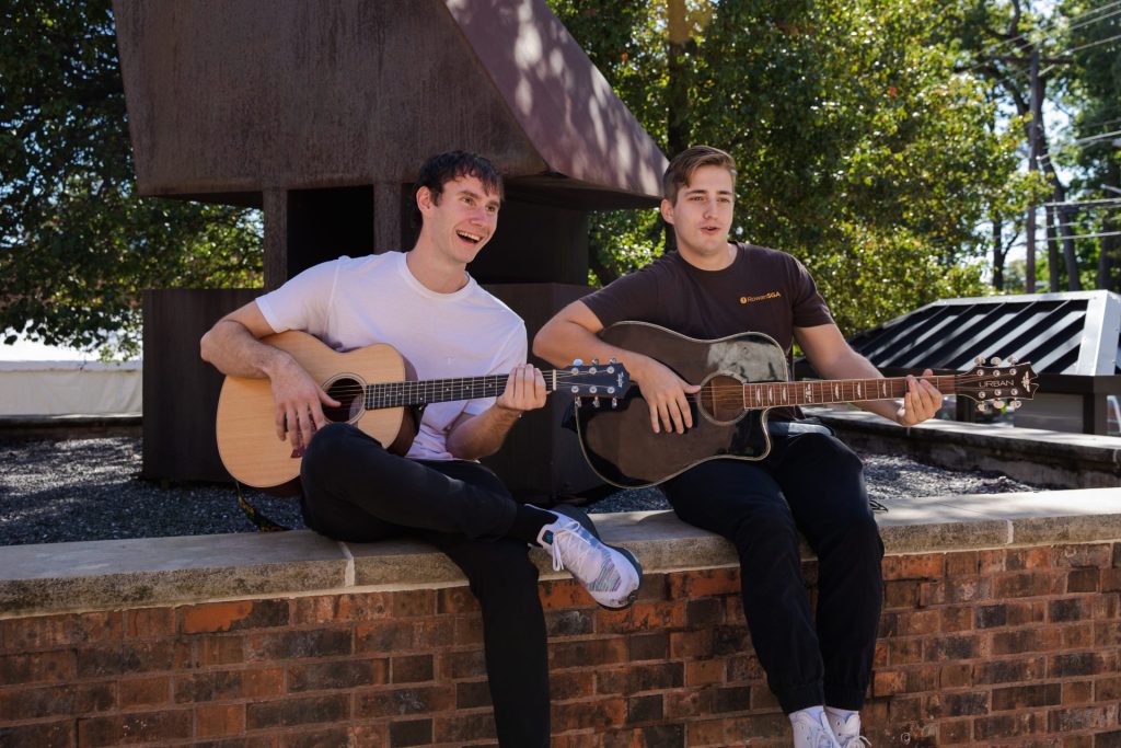 Two male students in 2023 play guitar outside the Student Center. 