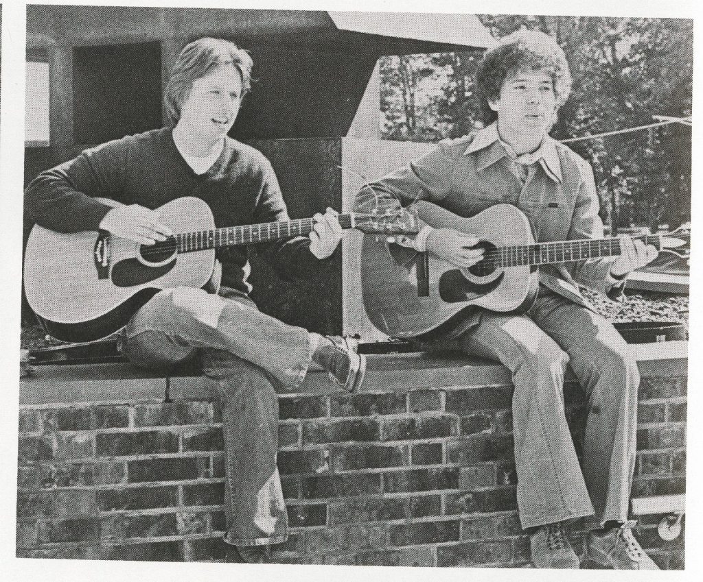 Two male students from the 1970s play guitar outside the Student Center. 