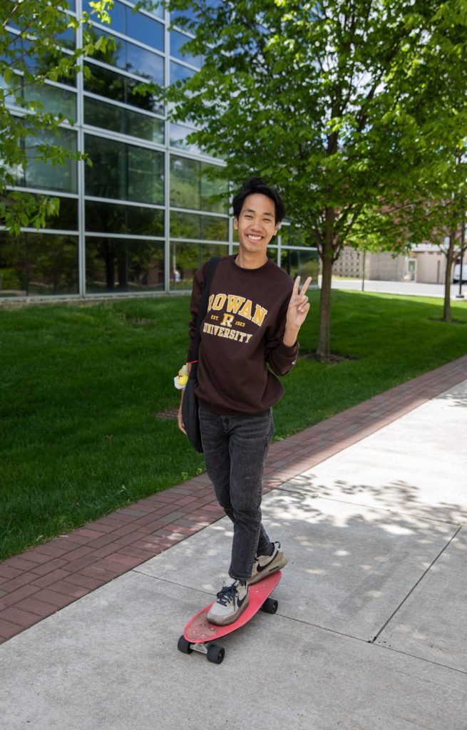 A male student skateboards in 2023 while flashing the peace sign. 