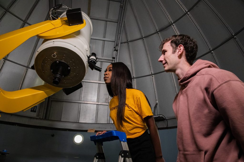 Two students in 2023 peer through a telescope. 