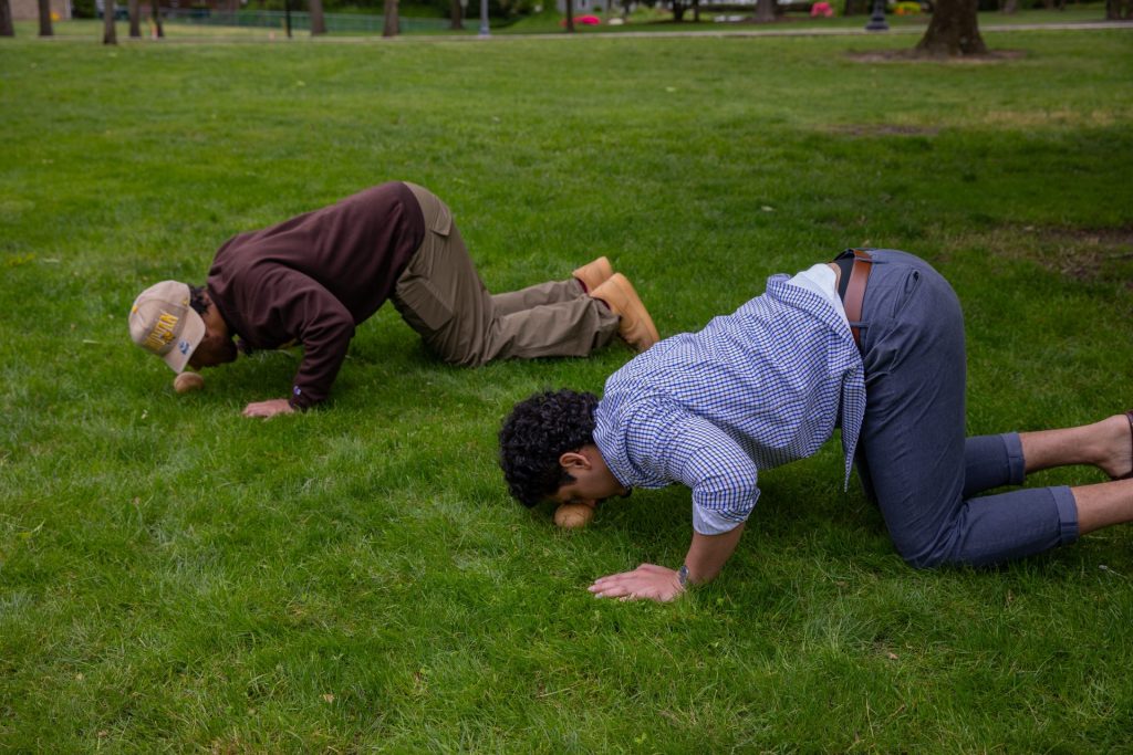 Two male students in 2023 push potatoes with their noses, crouched on the ground. 