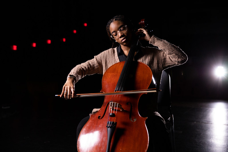 Aaliyah plays cello on a dark stage. 