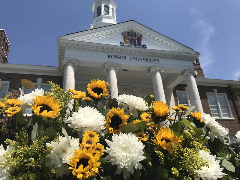 With white carnations and yellow and brown sunflowers in the foreground, we look up at the marble pillars of Rowan University's Bunce Hall. 