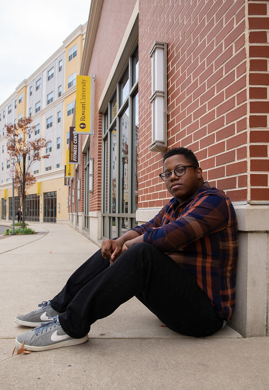 Sedrick sits against the brick wall of an academic building. 