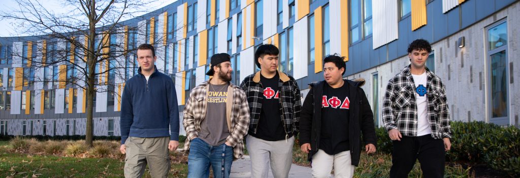Four Alpha Phi Delta fraternity brothers walk together past Holly Pointe Commons on a winter day.