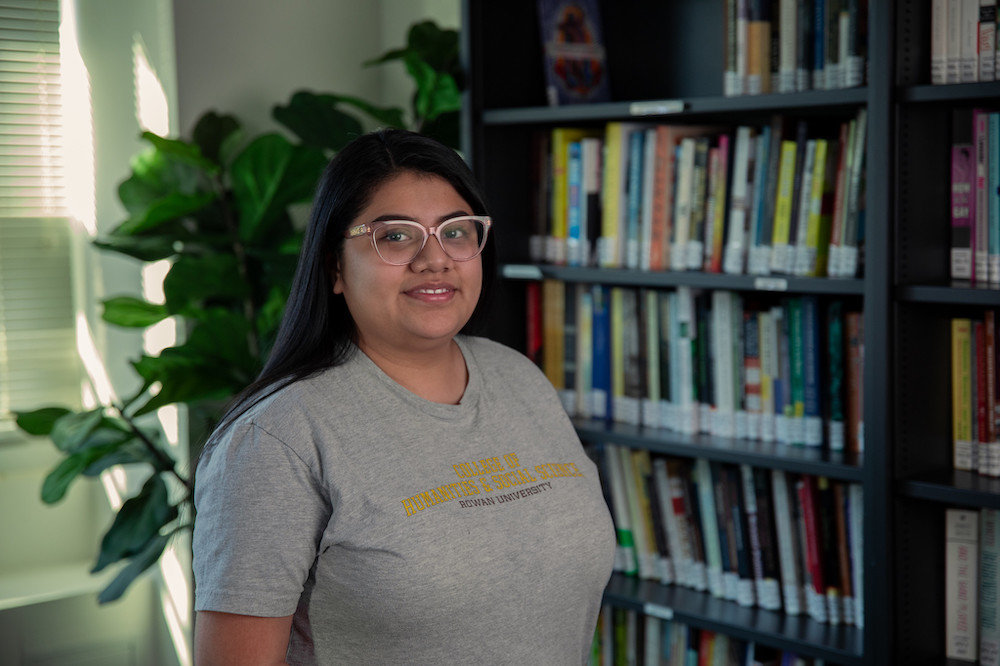 Rosa wears a Rowan University shirt with bookcases behind her. 